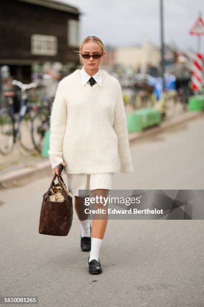 Guest wears black sunglasses, a white shirt, a black tie, a white latte fluffy oversized wool pullover, white suit shorts, a dark brown shiny leather...