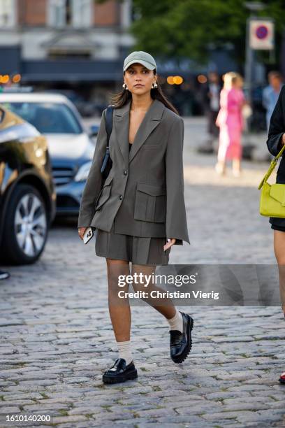 Guest wears cap, grey tailored blazer with side pockets, shorts outside Ganni during the Copenhagen Fashion Week Spring/Summer 2024 on August 10,...