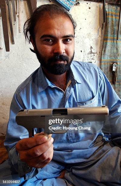 Zahid Shah, one of hundreds of gun manufacturers in the village of Darra Adam Khel, holds the gun he is making copied from a Chinese automatic pistol.