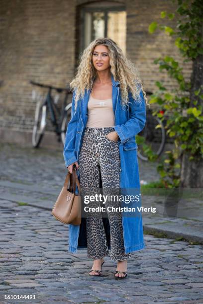 Emili Sindlev wears denim coat, brown Prada bag, animal print pants, sandals outside Ganni during the Copenhagen Fashion Week Spring/Summer 2024 on...