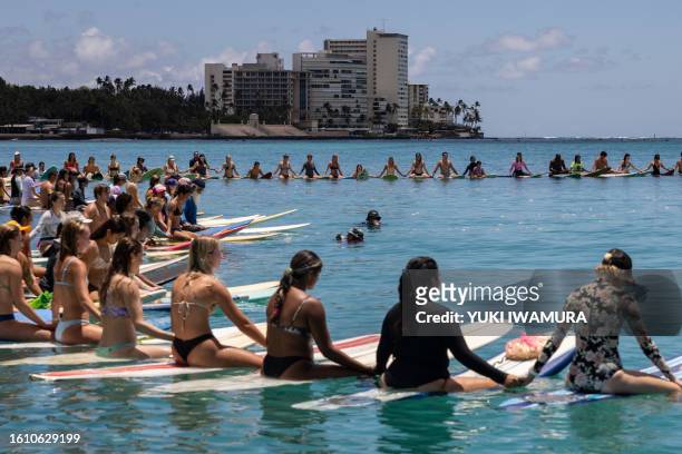 People hold hands during a community paddle out, organized by nonprofit Na Kama Kai for those affected by the Maui Fires, at Kuhio Beach, Honolulu,...