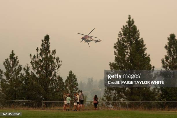 People gather to a lookout as a helicopter gathers water from Shannon Lake to fight the McDougall Creek wildfires in West Kelowna, British Columbia...