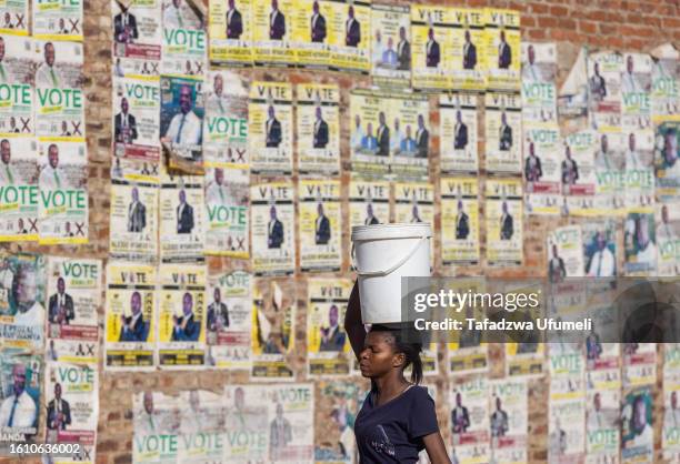 Woman carrying a container filled with water passes in front of a wall with campaign posters of participating candidates in the country's 2023...