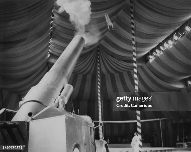 Person flying through the air in a big top tent about to land in a net as being shot out of a cannon at a circus or carnival.