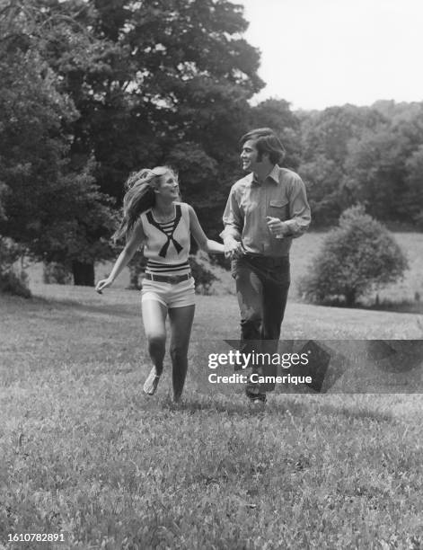 Young couple holding hands looking at each other happily while running through a field.