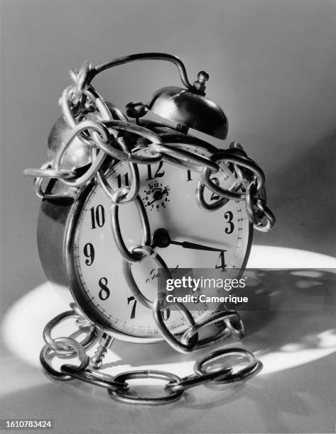 An image of an alarm clock with chains wrapped around it suggestive of time being stopped.