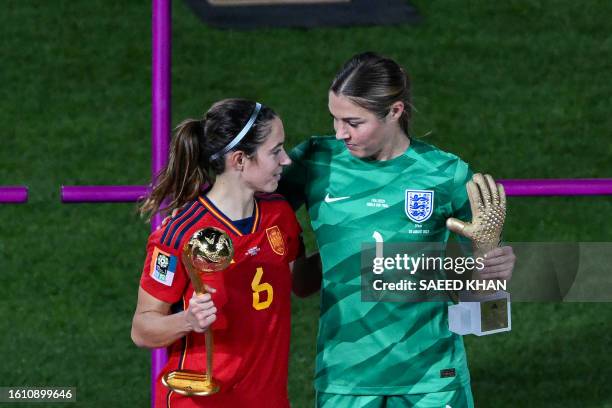 Spain's midfielder Aitana Bonmati holding the trophy on the podium for the FIFA Golden Ball Award embraces England's goalkeeper Mary Earps holding...