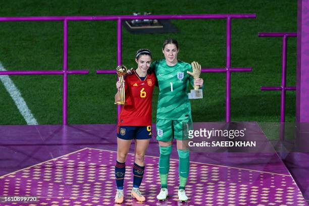 Spain's midfielder Aitana Bonmati holding the trophy on the podium for the FIFA Golden Ball Award embraces England's goalkeeper Mary Earps holding...