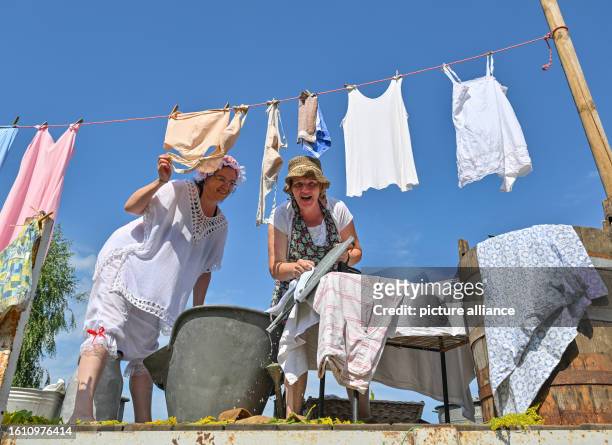 August 2023, Brandenburg, Burg: Two women show how laundry was washed 100 years ago, at the pageant in the Spreewald town of Burg. In the afternoon...