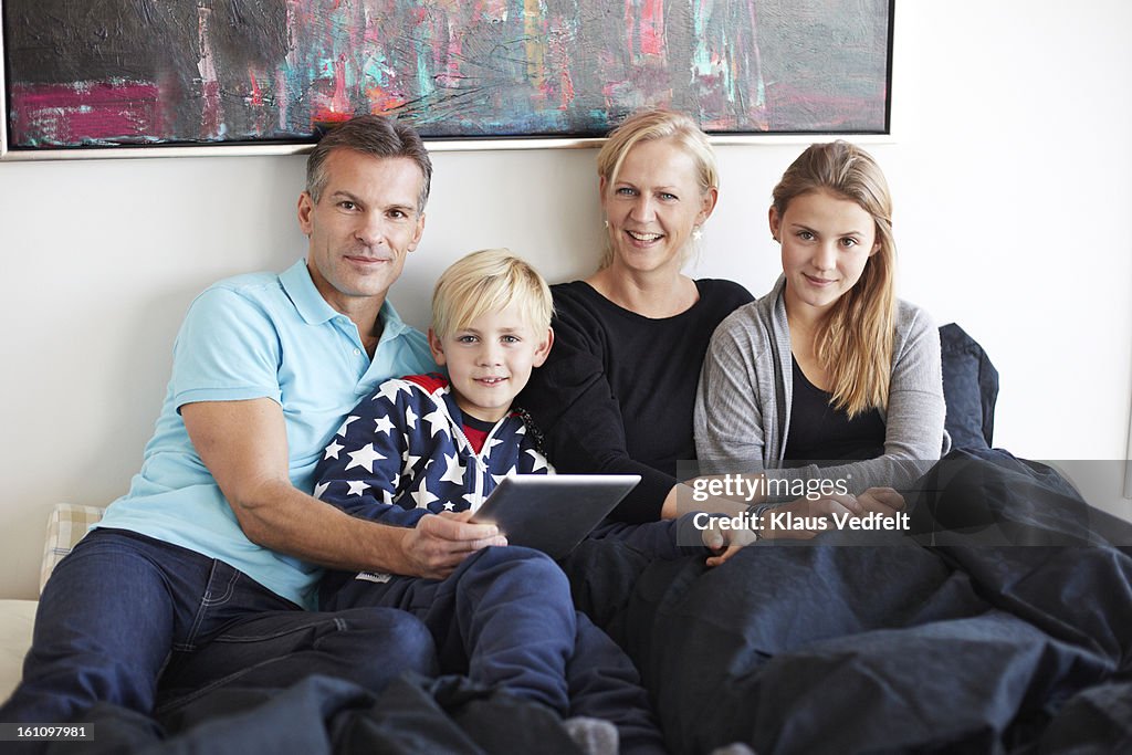 Family of 4 looking at tablet in bedroom
