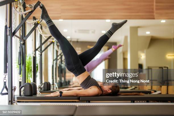 females in sportswear raising legs and doing hundred exercise on reformer bed during workout in light pilates studio. - metodo pilates foto e immagini stock