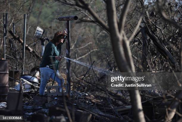 Resident, who did not giver her name, uses a garden hose to put out hot spots at a neighbor's house that was destroyed by wildfire on August 12, 2023...