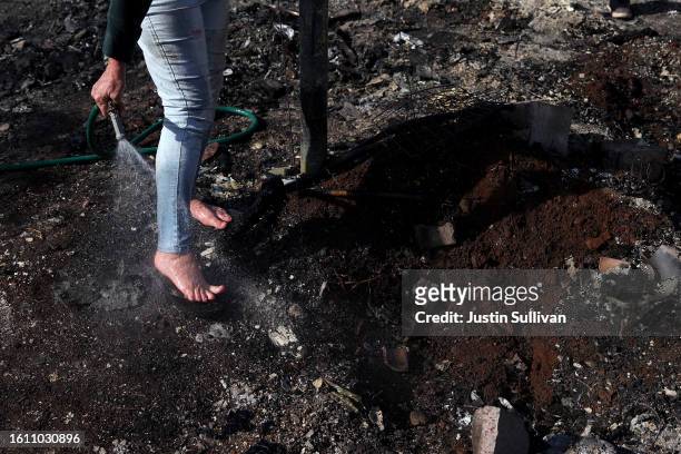 Resident, who did not giver her name, uses a garden hose to cool her feet after stepping hot embers at a neighbor's house that was destroyed by...