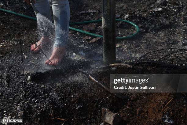 Resident, who did not giver her name, uses a garden hose to cool her feet after stepping hot embers at a neighbor's house that was destroyed by...