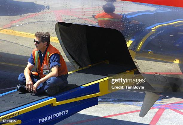 An American Airlines baggage handler sits on a baggage-feed conveyor belt as he awaits more luggage to load into the belly of a departing flight...