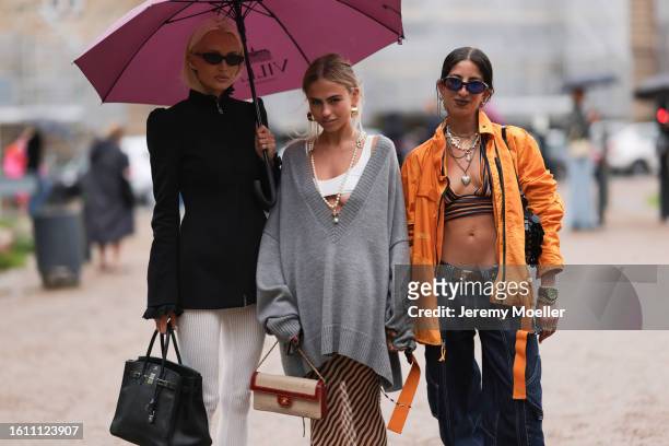 Selma Kaci is seen wearing lilac sunnies, Paco Rabanne golden earrings and necklaces, colorful striped bra top, oversized orange outwear jacket, low...
