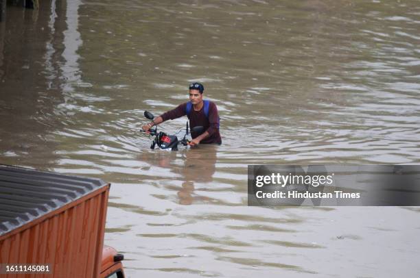 Commuter's two-wheeler stuck on the water-logged service lane amid heavy rain, at National Highway-48 near Narsinghpur village, on August 19, 2023 in...