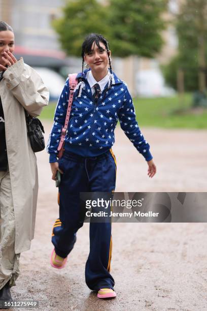 Guest is seen wearing blue silk jacket with white printed stars, navy blue Adidas jogging pants with orange stripes, pink Balenciaga Le Cagole bag...