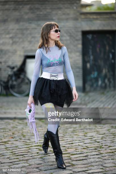 Guest wears black sunglasses, a pale blue tulle turtleneck / long sleeves with embroidered neon green and pink top, a black V-neck cropped top, a...