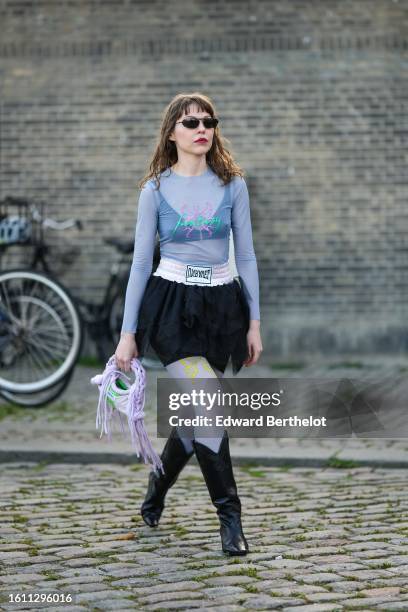 Guest wears black sunglasses, a pale blue tulle turtleneck / long sleeves with embroidered neon green and pink top, a black V-neck cropped top, a...