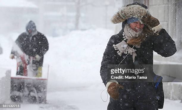Woman walks through the snow as a worker clears snow from a sidewalk in the Back Bay neighborhood during a lingering blizzard on February 9, 2013 in...