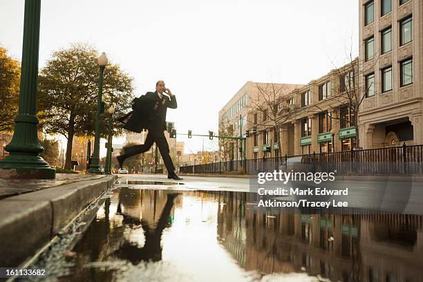 caucasian businessman jumping over urban puddle - pfütze stock-fotos und bilder