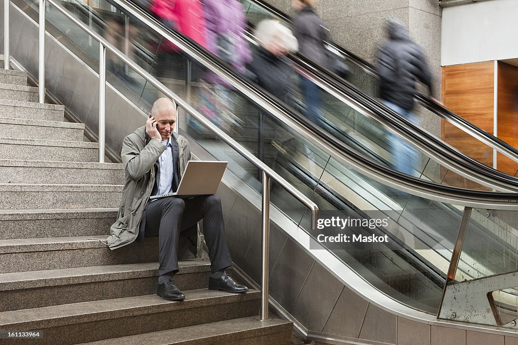 Man in stairs using laptop and cell phone