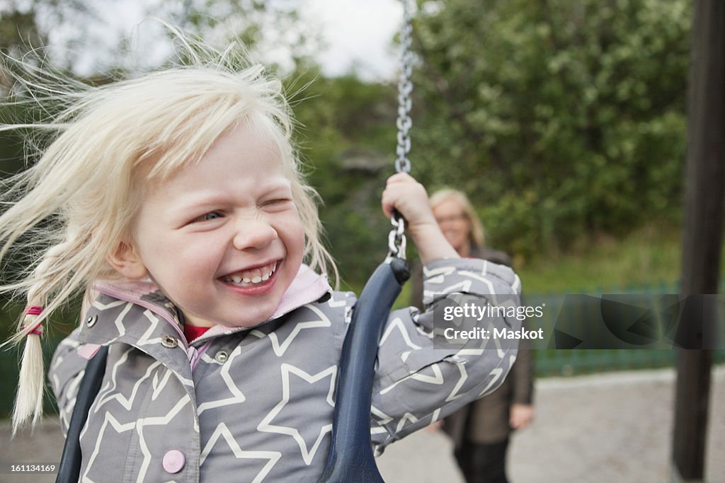 Cute cheerful baby (2-3) in swing with mother in the background
