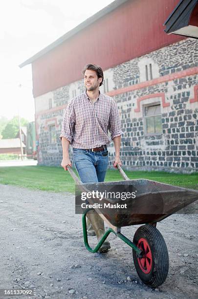 man pushing wheelbarrow - kruiwagen stockfoto's en -beelden