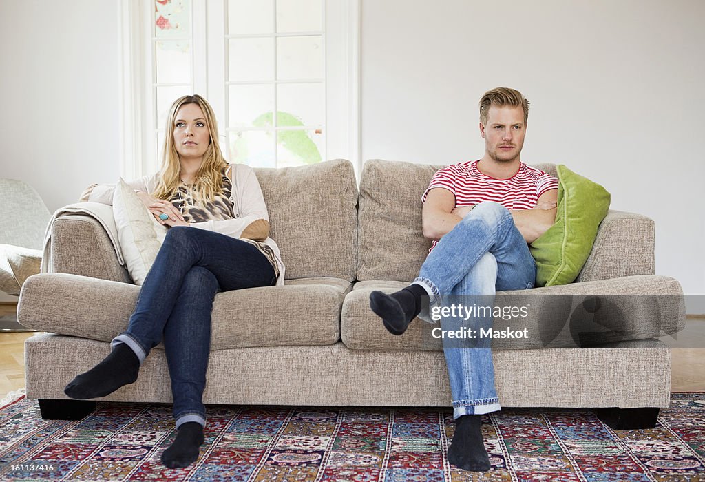 Couple looking away while sitting on sofa with arms folded