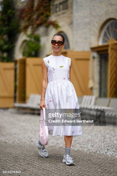 Guest wears brown sunglasses, a white with embroidered multicolored small pattern / sleeveless / midi dress, a pale pink satin handbag, gray socks,...