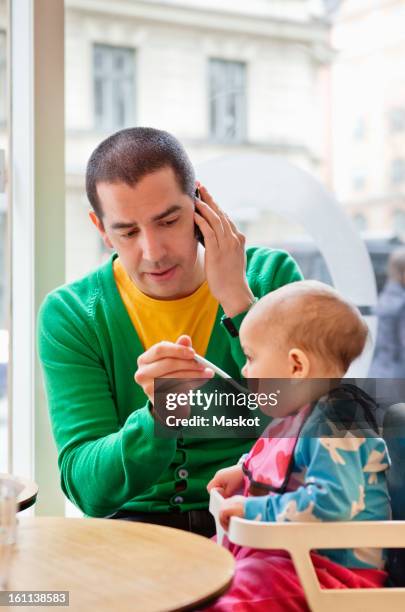 man feeding daughter (0-11 months) and talking in phone - 0 11 meses fotografías e imágenes de stock