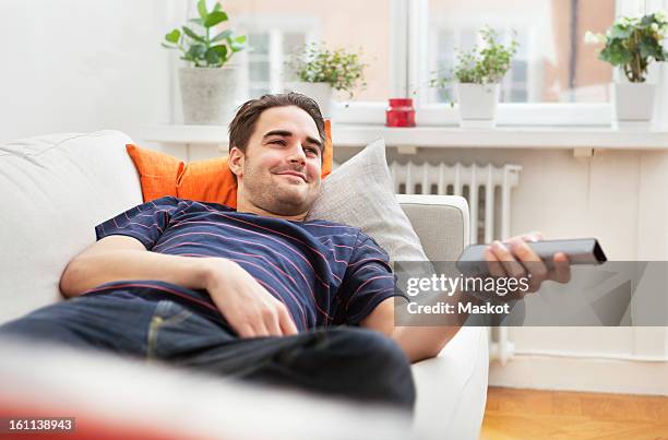 man lying in sofa - man watching tv foto e immagini stock