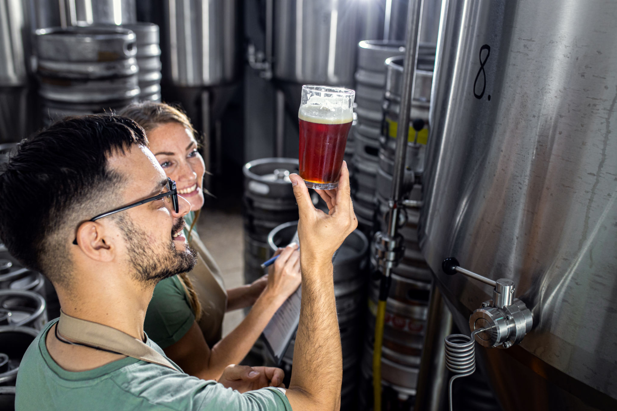 Man and woman working in craft brewery examining quality of the beer. Man and woman working in craft brewery examining quality of the beer.