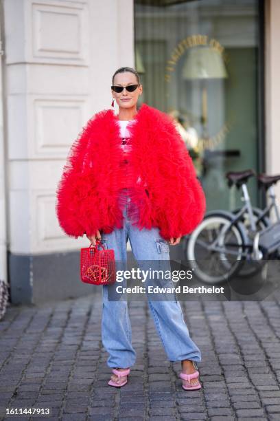 Guest wears black vintage sunglasses, a red and silver triangular pendant earrings from Prada, a white with black print pattern t-shirt, a neon red...