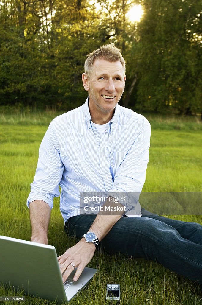 Man sitting in the grass with laptop and cellphone