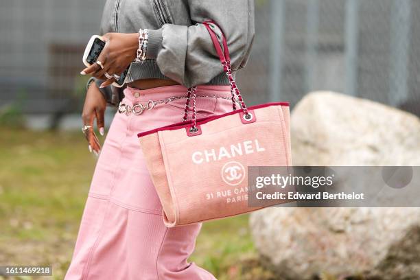 Guest wears a pale gray denim zipper bomber coat, a pale pink fabric / white print pattern tote bag from Chanel, a silver chain belt, a pale pink...