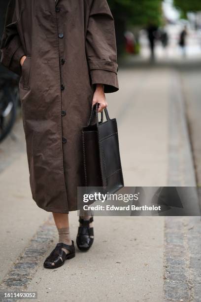 Guest wears a dark brown long coat, a black knees skirt, a black shiny leather large squared handbag, beige brown socks, black shiny leather large...