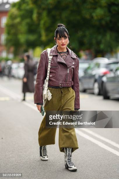 Guest wears silver earrings, a black and brown print pattern top, a burgundy shiny leather zipper biker jacket, a black and yellow micro houndstooth...