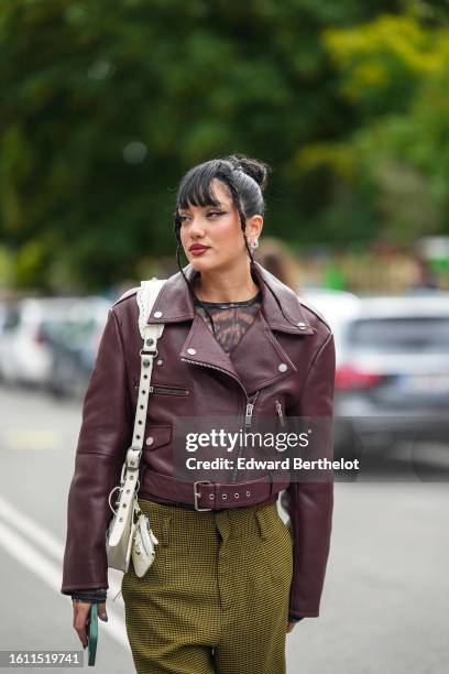 Guest wears silver earrings, a black and brown print pattern top, a burgundy shiny leather zipper biker jacket, a black and yellow micro houndstooth...