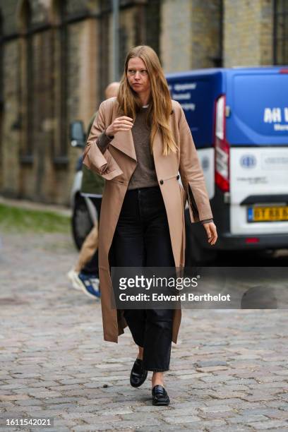 Guest wears a brown wool pullover, a beige brown long coat, black suit pants, black shiny leather loafers , outside Munthe, during the Copenhagen...