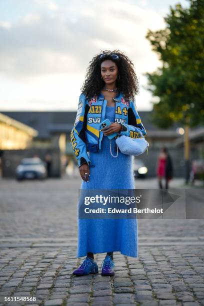 Guest wears silver earrings, a multicolored crystals necklace, a blue wool long dress, a blue shiny leather with yellow and white embroidered pattern...
