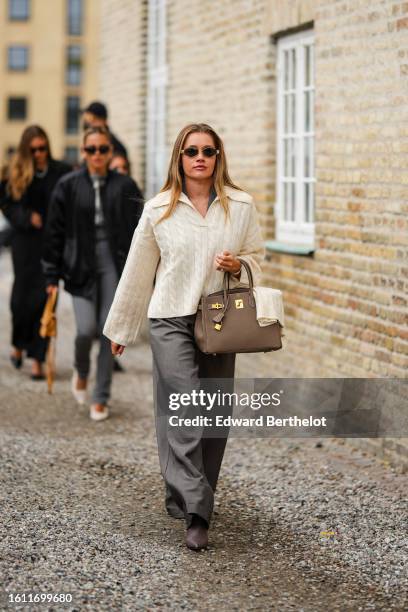 Guest wears gold earrings, a pale yellow braided wool polo shirt neck pullover, a brown grained leather Birkin handbag from Hermes, gray large suit...