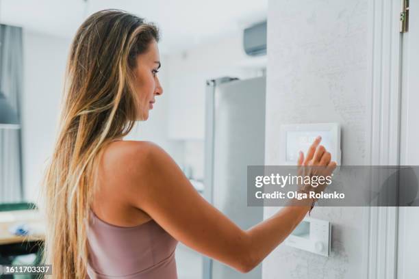 air conditioner and split system control at home. central heater. blonde woman adjusts the thermostat of the heat and cold elements at home - central air conditioner stock pictures, royalty-free photos & images