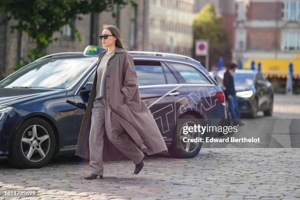 Guest wears black sunglasses, a pale gray wool hoodie pullover, a dark brown long coat, gray suit pants, black shiny leather block heels / ankle...