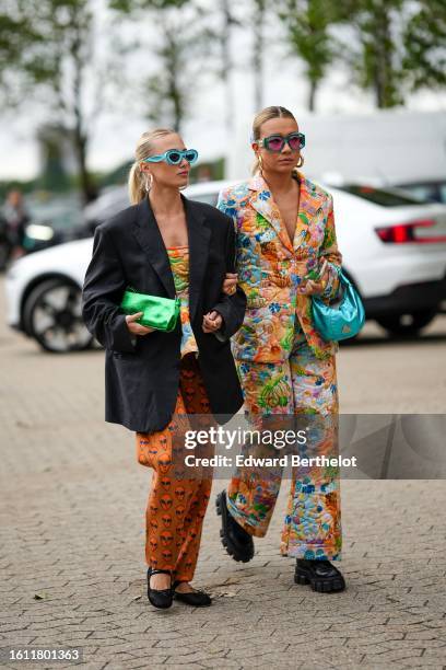 Guest wears flashy blue sunglasses, silver large earrings, a gold small necklace, a black oversized blazer jacket, a green shiny leather clutch, a...