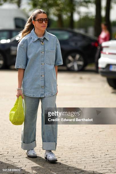 Guest wears black aviator sunglasses, a pale blue denim buttoned short sleeves shirt, pale blue denim rolled-up ankle large pants, a yellow cut-out...