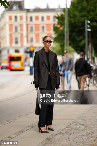 Guest wears black sunglasses, silver earrings, a black cropped top, a black oversized blazer jacket, a black high waist long skirt, a black shiny...