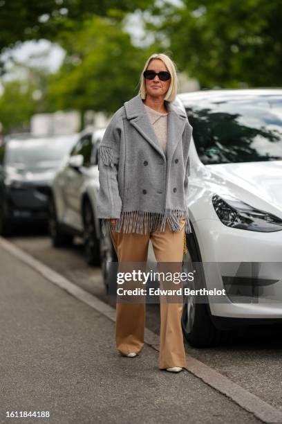 Guest wears black sunglasses, a beige t-shirt, a pale gray fringed wool coat, beige flared suit pants, beige pointed pumps heels shoes , outside Mark...