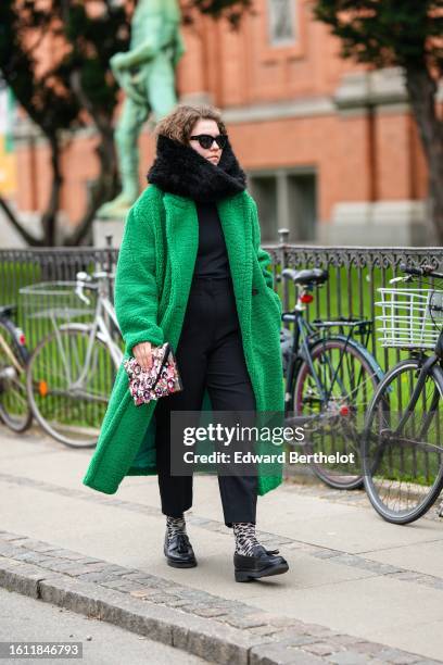 Guest wears black sunglasses, a black fur large scarf, a black t-shirt, black suit pants, a green fluffy long coat, a pink / silver / purple...